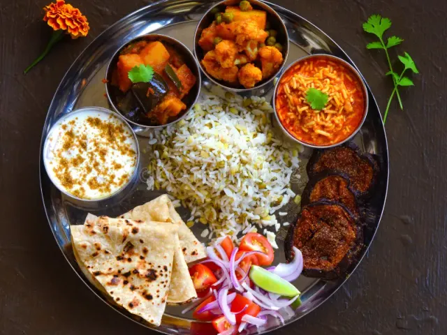 Overhead photograph of a fresh thali with chapati, rice, dal, sabzi, and salad on a steel plate